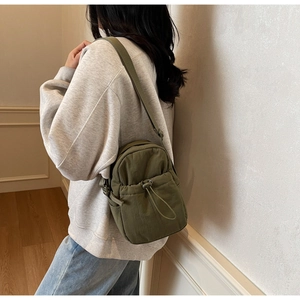 Detail of olive green nylon crossbody bag with drawstring pocket on a female model