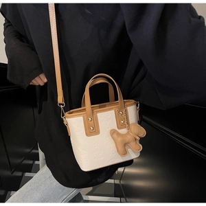 Detailaufnahme der weißen geprägten Beuteltasche mit braunem Griff und Hundeanhänger