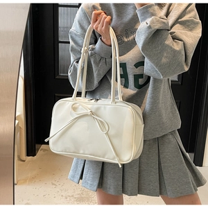 Close-up of white shoulder bag with bow detail and glossy synthetic leather texture