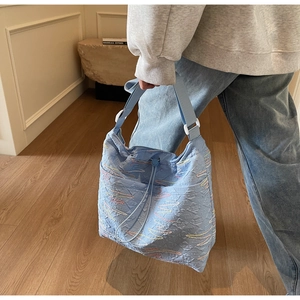 Detail of light blue quilted bucket bag with colorful embroidery and wide shoulder strap