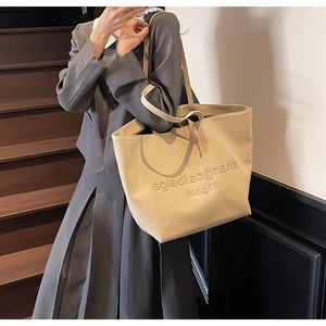 Close-up of beige canvas tote bag showing large capacity and embossed texture on stairs