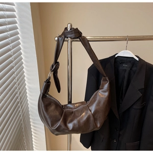 Detail of a dark brown pleated crescent bag with a decorative knotted shoulder strap