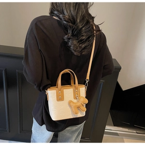 Detail der beigen Beuteltasche mit Sternprägung und einem braunen Hunde-Lederanhänger