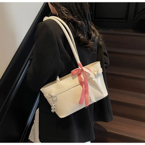 Détail du sac à bandoulière blanc crème avec nœud à carreaux rouges et breloque cœur