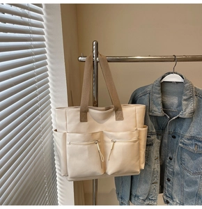 Detail of off-white canvas tote bag with functional zipper pockets and brown straps