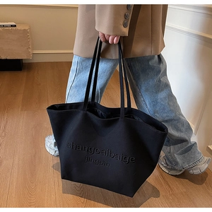 Detail of black canvas tote bag with embossed lettering and dual shoulder straps