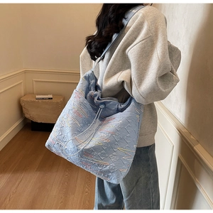 Detailed side view of a large light blue quilted canvas tote bag with wavy embroidery