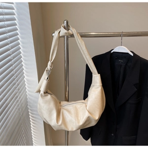 Detail of a creamy white crescent shoulder bag with stylish knotted strap design