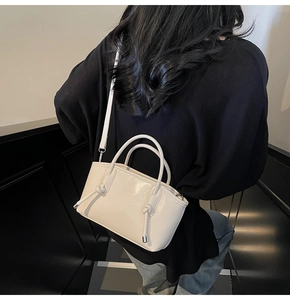 Dettaglio di una borsa tote beige con fibbia metallica e tracolla indossata da una modella