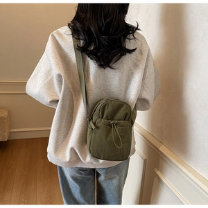 Olive green nylon crossbody bag detail with drawstring and adjustable strap on a model