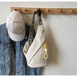 Detail of a beige canvas chest bag with a yellow carabiner clip and lettered strap