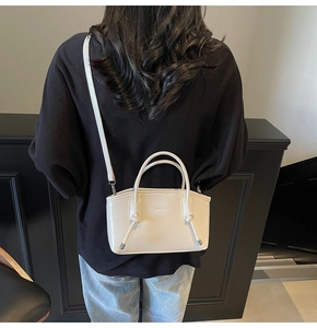 Dettaglio della borsa tote bianco crema con manico annodato e logo del marchio indossata da modella