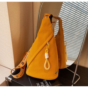 Detail of a mustard yellow nylon chest bag featuring a diagonal zipper and patterned strap