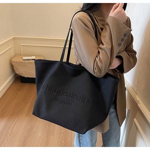 Detail of black canvas tote bag featuring embossed lettering and durable shoulder straps