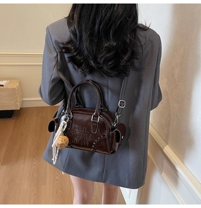 Detail of dark brown patent leather Boston bag with embossed logo and strawberry charm