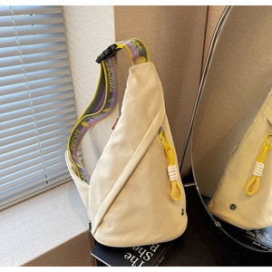 Detail of cream nylon crossbody bag with contrast straps and yellow zipper pulls