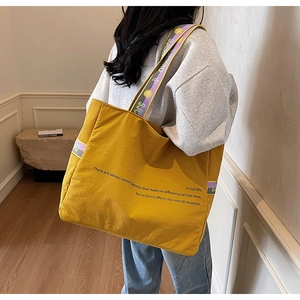 Détail du sac fourre-tout en nylon jaune avec large bandoulière violette et texte imprimé