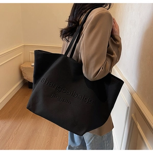 Detail of embossed lettering on a large black canvas tote bag for stylish women's commuting
