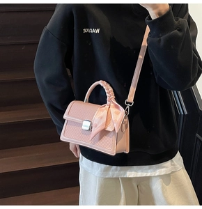 Détail d'un sac bandoulière rose avec texture tressée et poignée décorée d'un foulard