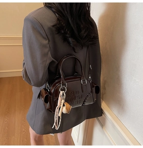 Detail of dark brown glossy patent leather Boston bag with 3D embossed letters and charm