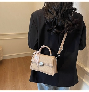 Détail d'un sac à main beige tressé avec foulard en soie porté par un mannequin en noir