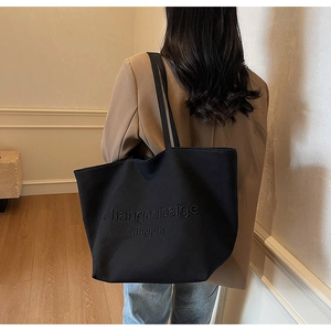 Detail of black canvas tote bag showing the embossed texture and long shoulder straps