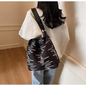 Detailed view of black canvas bucket bag with wavy embroidery on model's shoulder