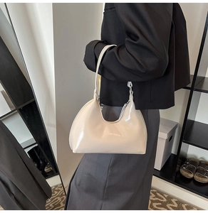Side view of a creamy white glossy leather hobo bag worn as a shoulder bag