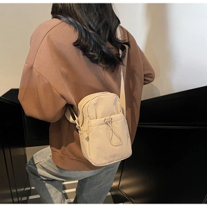Close-up of minimalist cream nylon crossbody bag featuring a functional drawstring pocket