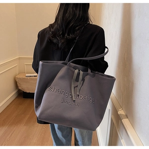 Detail of grey-blue canvas tote bag featuring letter print and decorative drawstrings