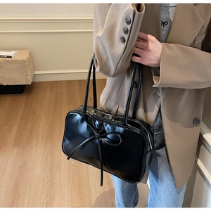 Detail of black glossy leather tote bag with bow decoration shown on shoulder