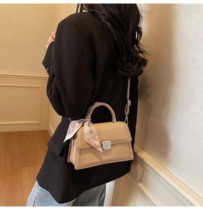 Détail du sac beige avec texture tissée, fermoir rotatif et foulard à coeurs roses