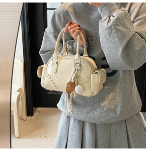 Detail of cream shoulder bag with baseball stitching and themed pendant accessory