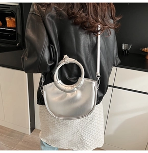 Silver crescent bucket bag with round metal handle and shiny leather texture in hand