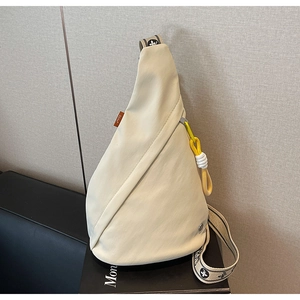 Detail of a beige teardrop chest bag with neon yellow zipper pull and patterned strap