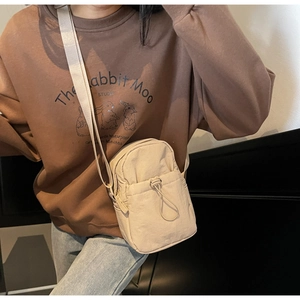 Detail of a beige nylon crossbody bag with drawstring front pocket and fabric strap