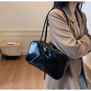 Detail of glossy black shoulder bag with a ribbon bow and mirror-like finish