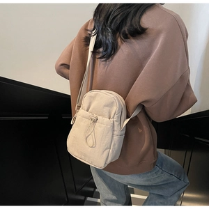 Detail of a minimalist beige nylon crossbody bag with drawstring pocket on a model
