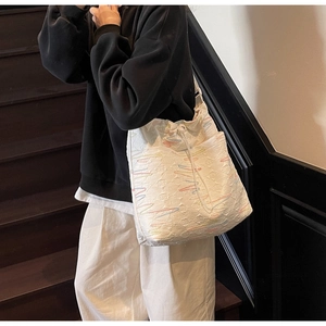 Detailed view of white quilted tote bag with colorful wave embroidery and drawstring closure