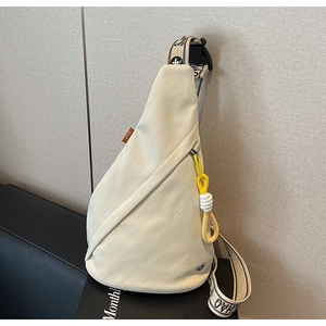 Close-up of minimalist cream chest bag featuring lettered strap and yellow knotted zipper
