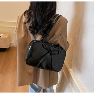 Detailed back view of a glossy black bow-knot tote bag worn with a chic tan blazer
