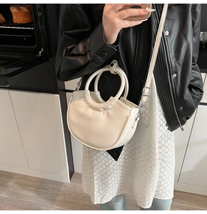 Detail of a creamy white crescent bag with silver hardware in a modern kitchen setting
