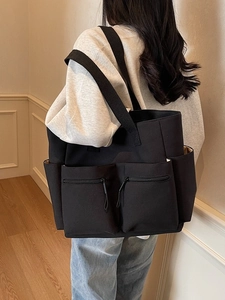 Minimalist black canvas tote bag with multi-pocket design shown on model's shoulder