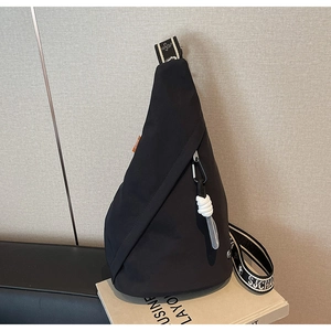 Detail of a black triangular crossbody bag with white cord zippers and a patterned strap