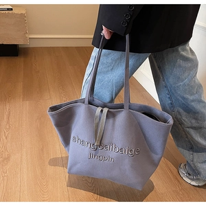 Close-up of minimalist dusty blue canvas tote bag with letter embroidery and handle detail