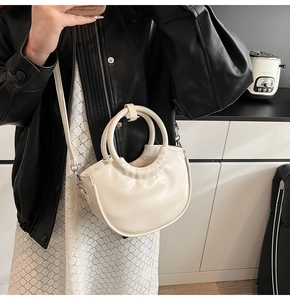 Detail of a creamy white half-moon bag with a round handle and sleek glossy finish