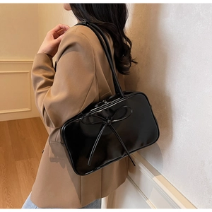 Detail of black glossy leather shoulder bag featuring a large decorative bow