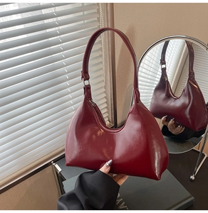 Detail of dark red crescent shoulder bag with smooth glossy finish and metal zipper