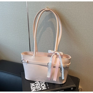 Détail d'un sac cabas rose clair avec nœud à carreaux et pendentif cœur sur un livre