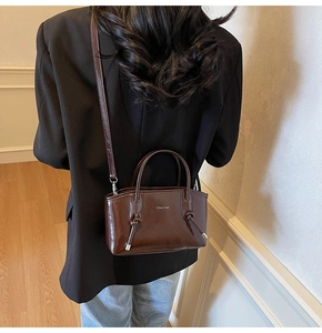 Dettaglio borsa tote in pelle marrone cioccolato lucida con logo argento e tracolla annodata